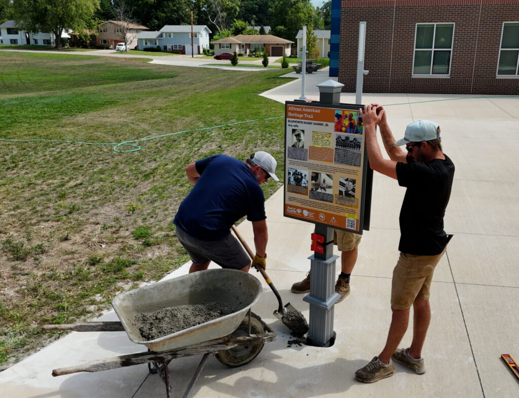 Workers install Macon County African American Heritage Trail sign outside a Decature area school