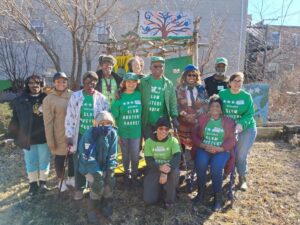 Group of people wearing green t-shirts witht the words "Historic Slum Busters Garden," standing in a community garden space.